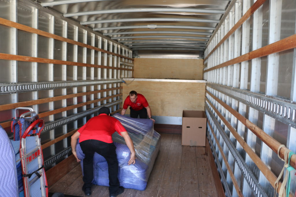 two men placing a wrapped up couch in a moving truck