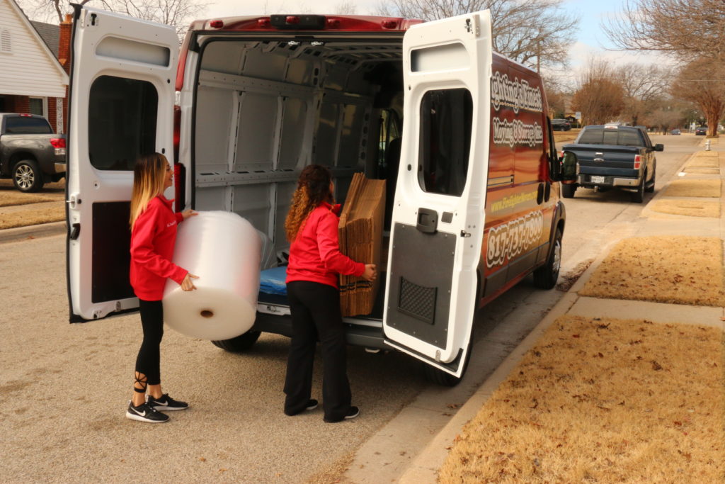 two women carrying boxes and bubble wrap out of moving van